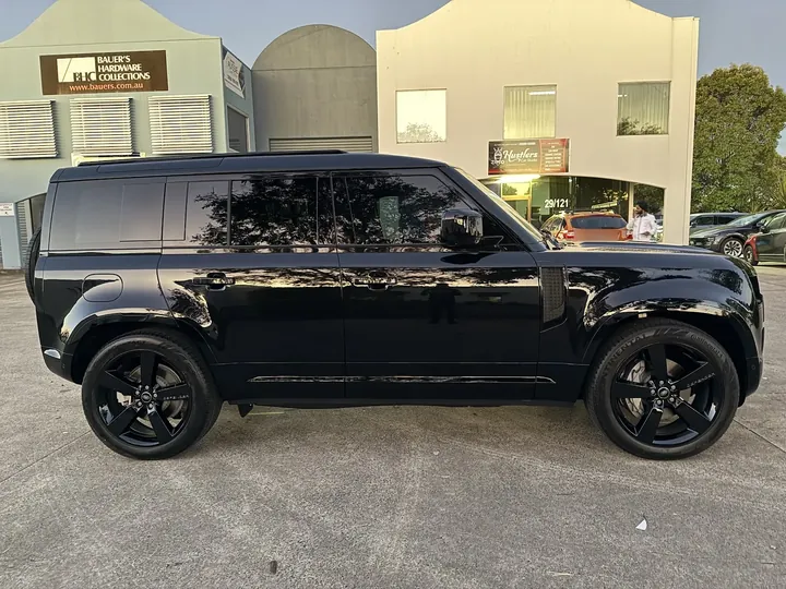 Black boxy SUV photographed side-on with buildings reflected in the glossy panels.