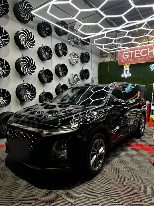 Black SUV in the studio bay under hexagonal ceiling lights, reflecting them on the bonnet.