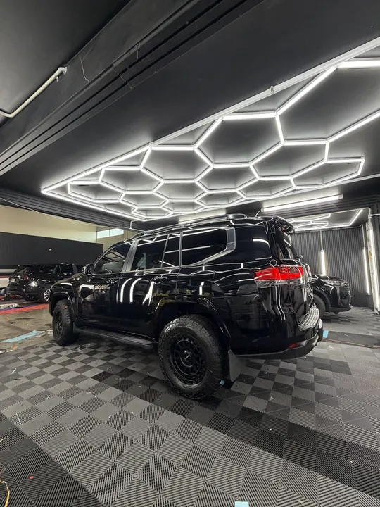 Black SUV in the studio bay seen from the rear, ceiling lights reflecting in the paint.