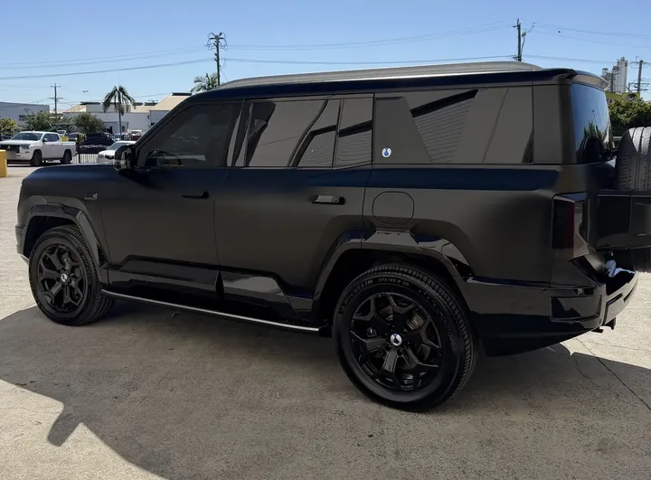 Matte black SUV seen side-on from the rear three-quarter with black alloy wheels.