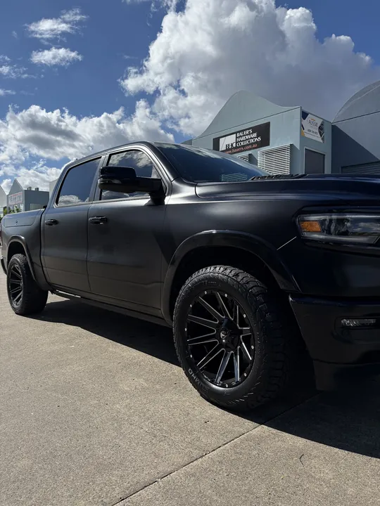 Matte black ute photographed from the front three-quarter with black wheels and a blue sky.