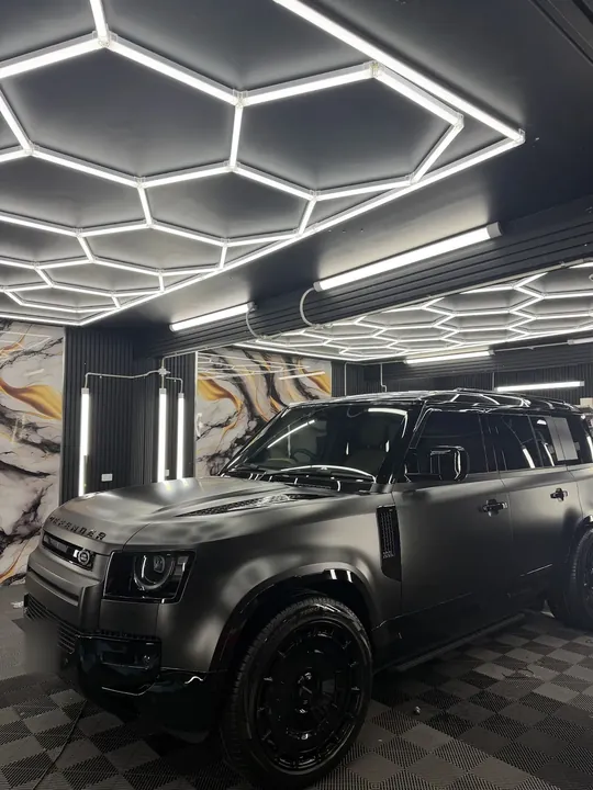 Matte dark grey SUV in the studio bay under hexagonal ceiling lights.