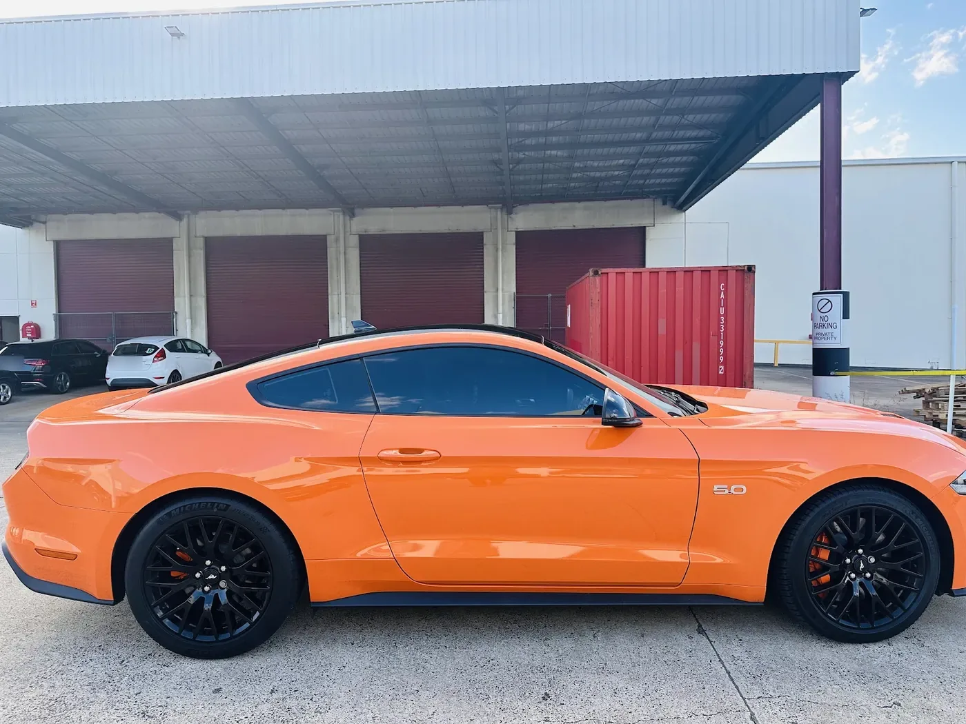 Orange coupe parked side-on outdoors with deep gloss paint and black alloy wheels.