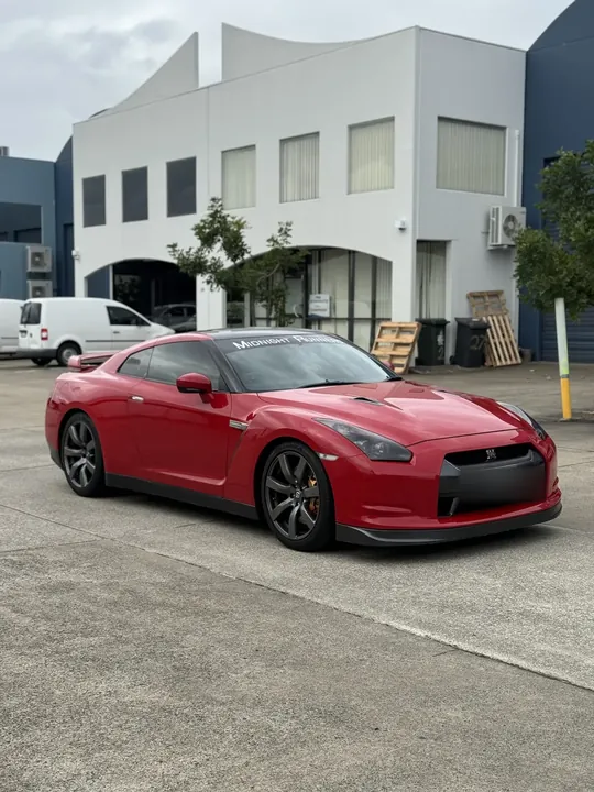 Red sports coupe parked in front of a building, bonnet and roof showing strong reflections.