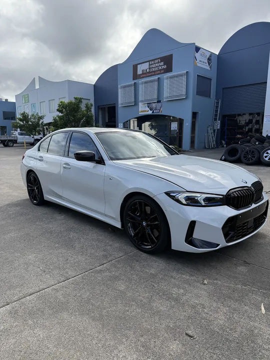 White sedan seen from the front three-quarter angle with black wheels in a car park.