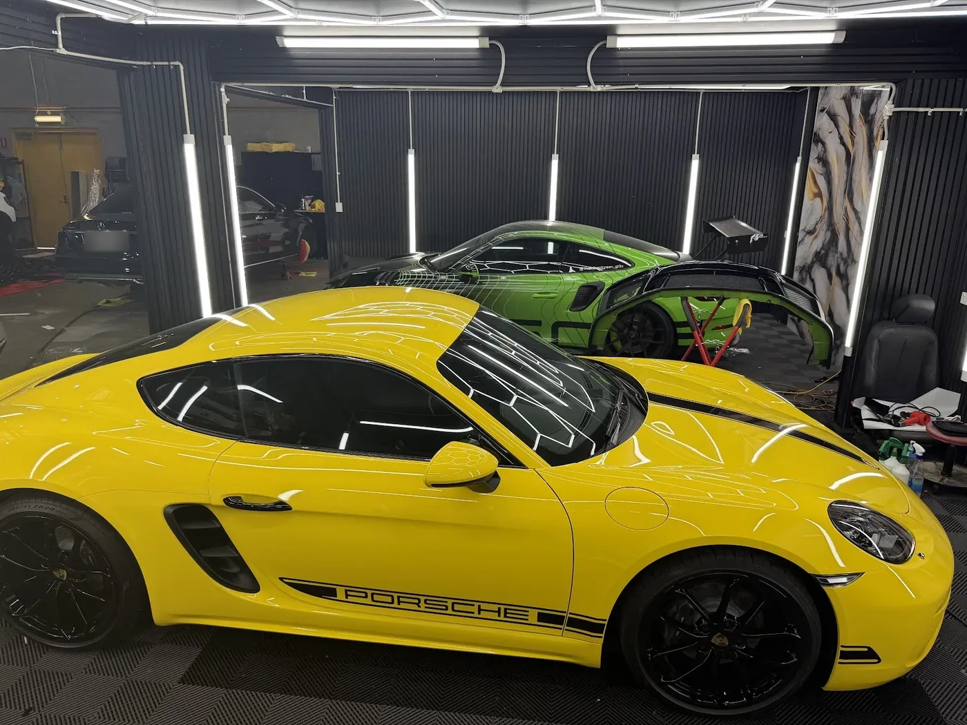 Yellow coupe in the studio bay with bright ceiling lights reflecting along the bonnet.